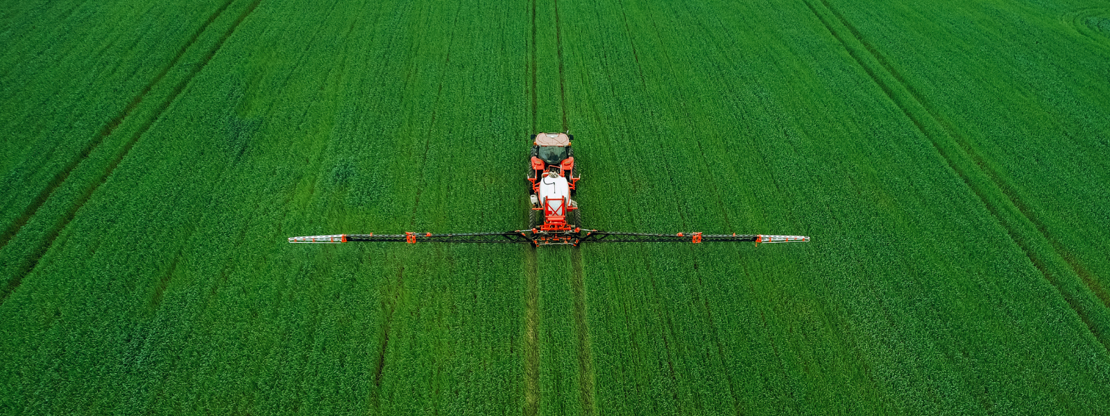 Tractor die een groen veld met pesticide bewerkt van bovenaf